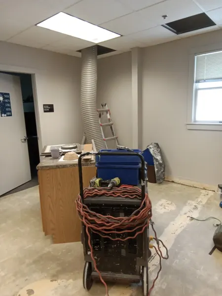 Vacuum hose run up through a removed ceiling tile while cleaning air ducts in an office.