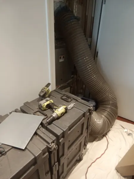 Vacuum hose connected to a closet air handler with tools staged on Armstrong's equipment cases.