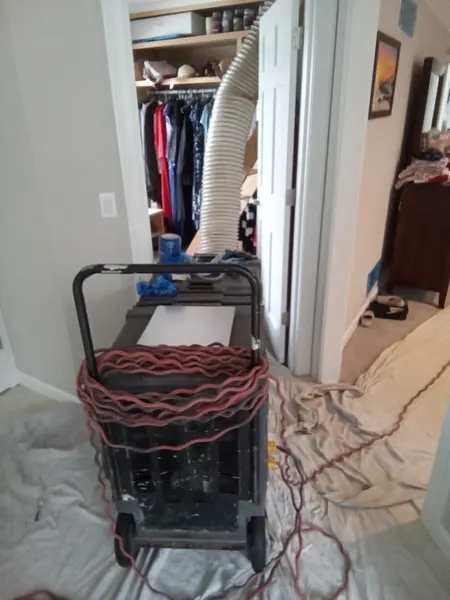 Duct-cleaning equipment staged on drop cloths that protect a bedroom's carpet while the vacuum hose runs into the closet.