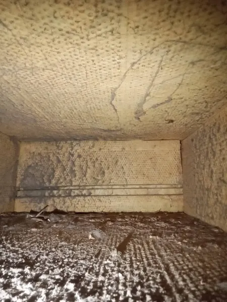 Dust and lint collecting on the floor of a fiberglass duct-board trunk before cleaning.
