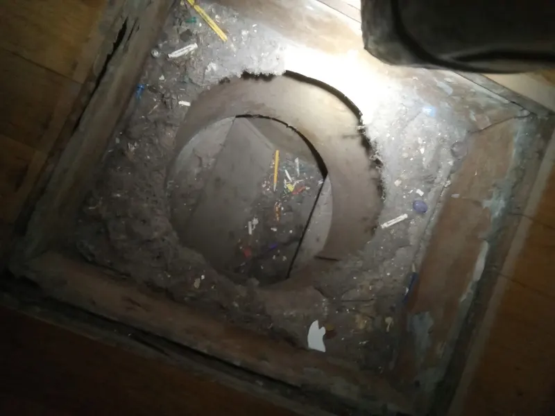 A floor register opening filled with dust and dropped household debris before Armstrong's cleaning.