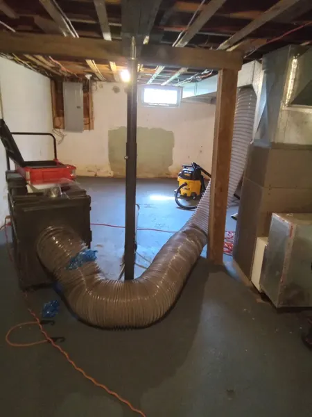 Armstrong's negative-air vacuum machine and flexible hose set up in a basement for air duct cleaning.