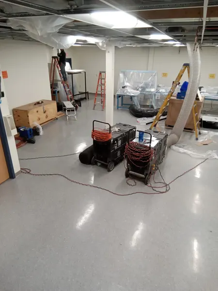 Armstrong crew cleaning overhead ductwork through a suspended ceiling, with vacuum machines and plastic sheeting protecting the space.
