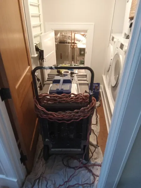 Portable duct-cleaning vacuum positioned on protective floor coverings outside a laundry room.
