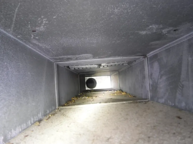 Dust film and scattered debris inside a sheet-metal return air duct before Armstrong's cleaning.