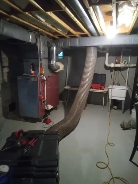 Armstrong's large vacuum hose connected to a basement furnace during whole-home air duct cleaning.