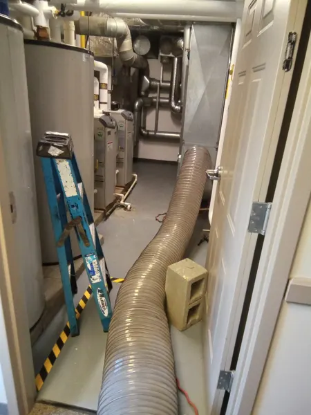 Negative-pressure vacuum hose routed through a utility room past the water heaters to reach the home's ductwork.
