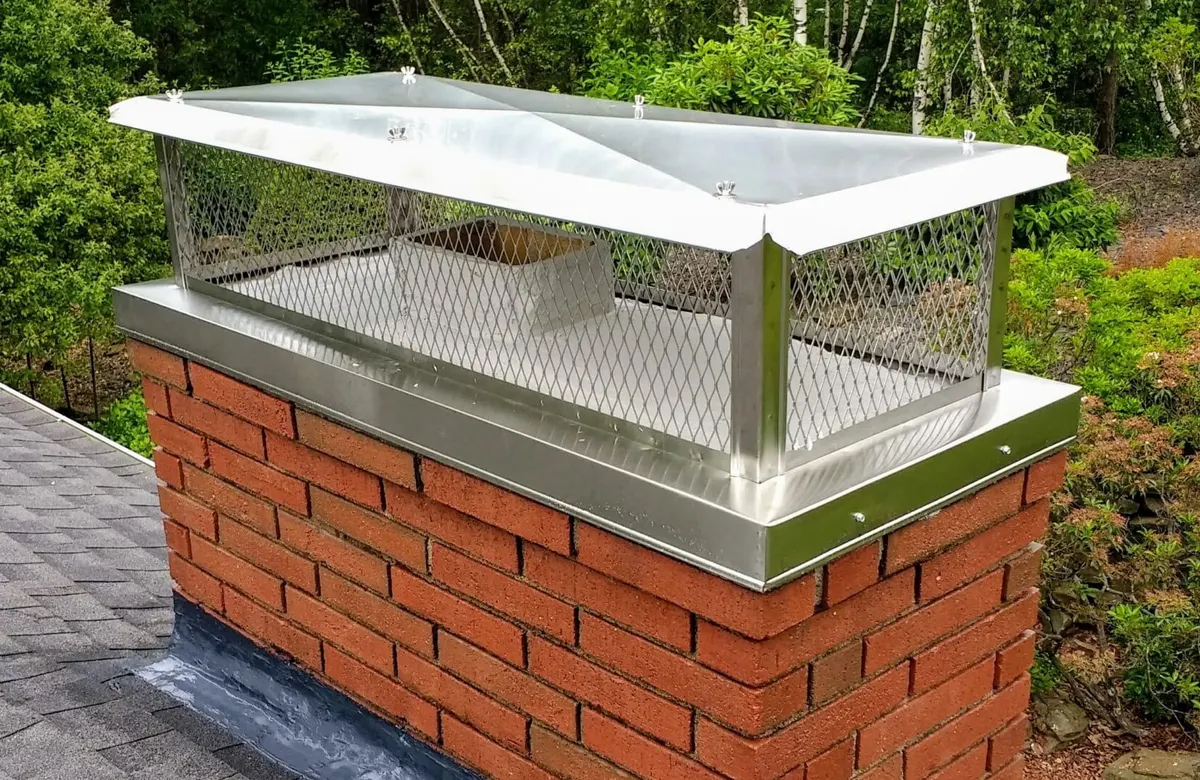 Long stainless steel flat-top chimney cap with a skirt that wraps the chimney's upper brick course.
