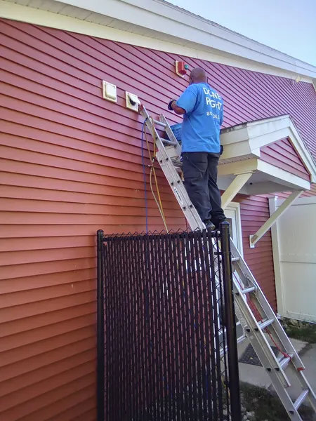 Technician on an extension ladder servicing high wall dryer vents at a red-sided condominium.