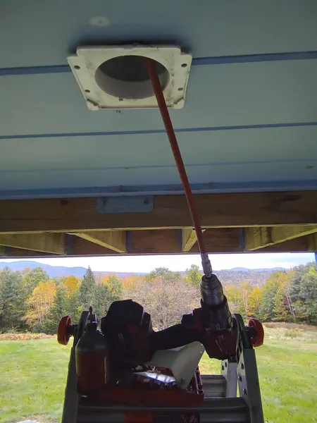 Drill-powered rotary rod cleaning a dryer vent that exits through a porch ceiling soffit.