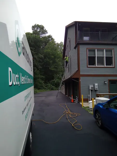 Armstrong Duct, Vent & Chimney truck on site as a technician climbs a tall ladder to an upper-floor dryer vent.