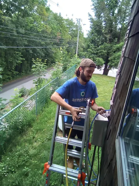 Armstrong technician on a ladder cleaning a dryer vent on a cedar-shake exterior wall.