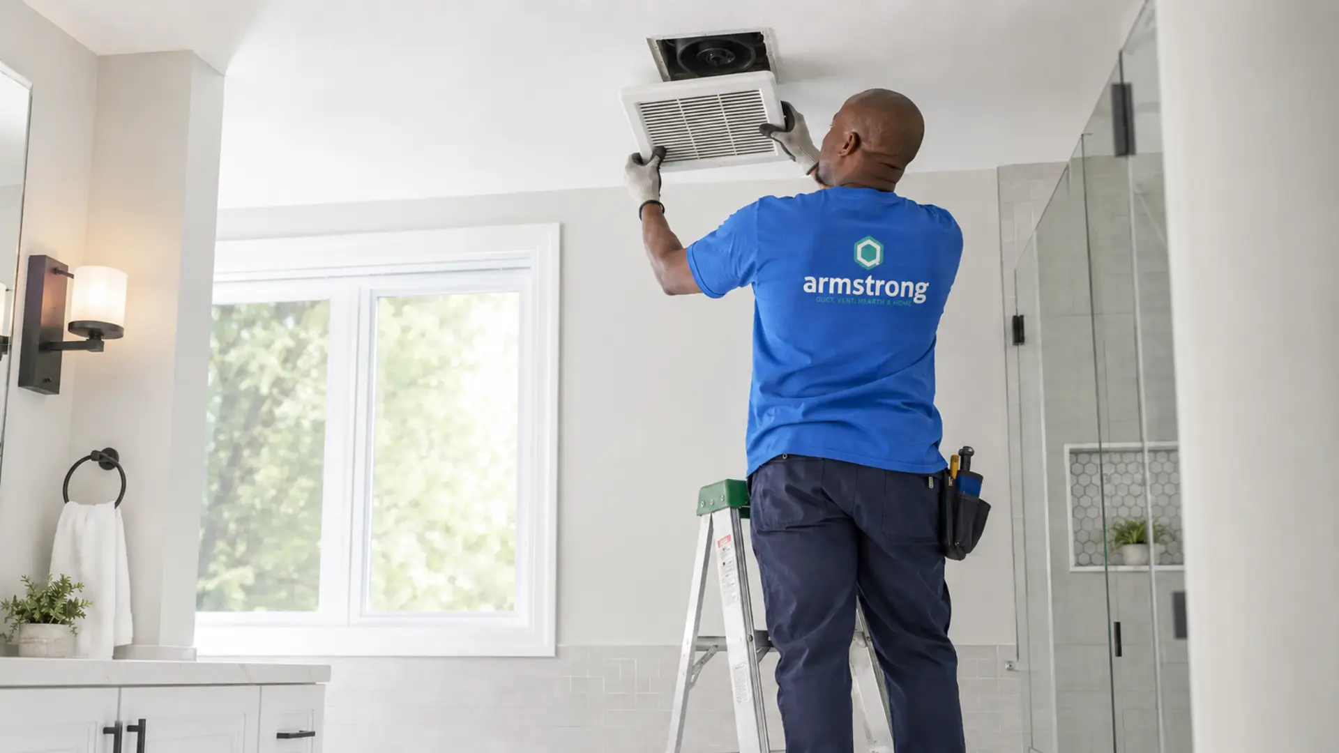Technician cleaning a bathroom exhaust fan grille in a New Hampshire home